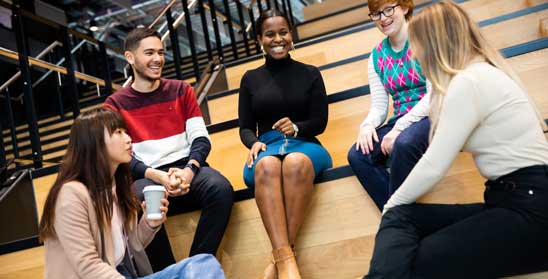 Group of students sat on steps chatting and smiling