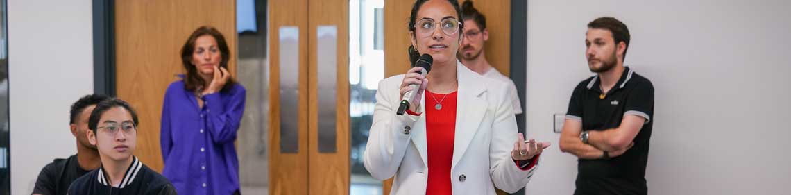 Lady stood with a microphone in a room of people